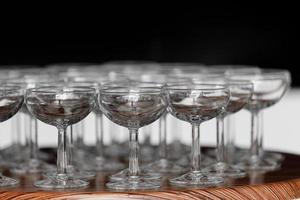 muchas elegantes copas vacías de vino o champán en la mesa de madera en el día de la boda. conjunto de vasos vacíos en blanco que se muestran en filas. preparación para las vacaciones foto