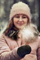 Christmas lights are bright splashes burning in the hands of a blurry happy woman in the park. Sparkler. Emotions, New Year's mood.Winter holidays photo