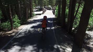 A boy rides his mountain bike on a paved trail in the woods.