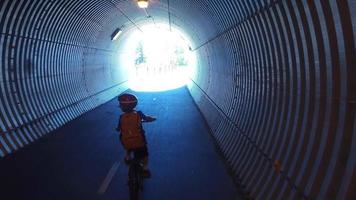 A boy rides his mountain bike through a tunnel on a paved trail in the woods. video