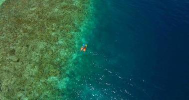 Vista aérea de drone de una pareja de hombre y mujer buceando sobre un arrecife de coral de una isla tropical.