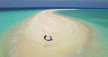 Vista aérea de un hombre y una mujer desayunando en la playa de un banco de arena de una isla tropical. video