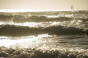 Olas del océano bajo la puesta de sol con forma de velero en el horison foto