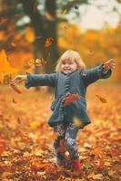 Niña feliz lanzando hojas amarillas de otoño en el aire en el parque, fondo de otoño foto