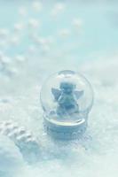 Small snow globe with angel figurine and snow winter background with copy space