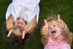 dos niñas recostadas en el césped, riendo y mostrando los pulgares hacia arriba foto