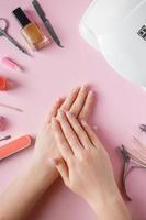 procedimiento de spa para el cuidado de las uñas en un salón de belleza. manos femeninas y herramientas para manicura sobre fondo rosa. concepto de cuidado corporal.