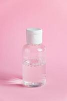 Bottle with micellar cleansing water on pink background. Skin care concept. photo