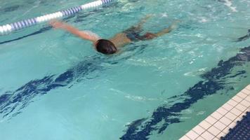 um menino nada em estilo livre durante as aulas de natação em uma piscina. video