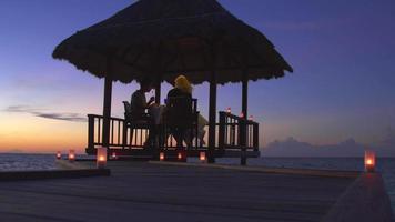una pareja de hombre y mujer cenan y cenan en una cabaña en la playa de una isla tropical. video