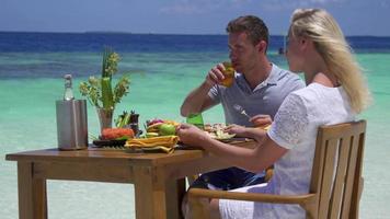 un hombre y una mujer desayunan en la playa de una isla tropical.