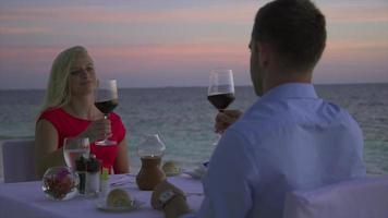 un hombre y una mujer cenan y beben vino en la playa de una isla tropical. video