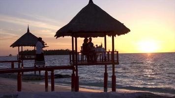una pareja de hombre y mujer cenan y cenan en una cabaña en la playa de una isla tropical. video