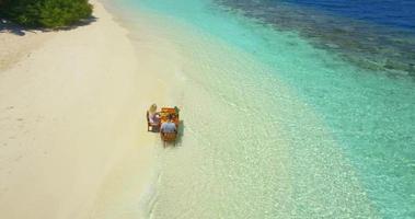 Vista aérea de un hombre y una mujer desayunando en la playa de una isla tropical. video