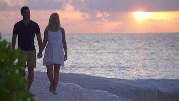 una pareja caminando por la playa al atardecer en un hotel resort de una isla tropical.
