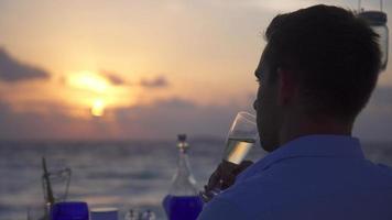una pareja de hombres y mujeres cenan y beben champán en la playa de una isla tropical. video