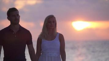 um casal caminhando na praia ao pôr do sol em um hotel resort em uma ilha tropical. video
