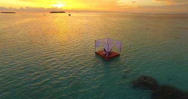 Vista aérea de un hombre y una mujer cenando en una balsa flotante al atardecer.
