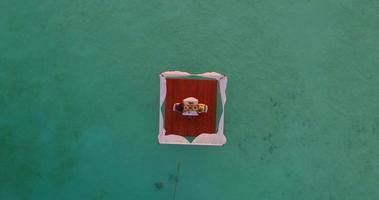 Vista aérea de un hombre y una mujer cenando en una balsa flotante al atardecer.