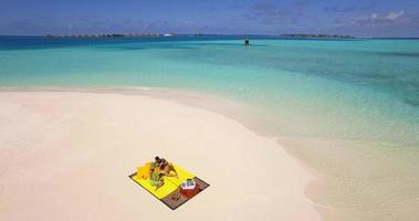 Vista aérea de drone de una pareja de hombre y mujer con una comida de picnic en una playa de una isla tropical. video