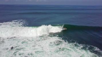vista aerea del drone di un uomo che fa surf su un'onda in indonesia.