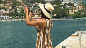 una donna con un cappello scatta foto mentre viaggia in una località turistica di lusso in italia, europa. video