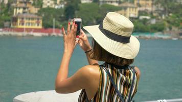 Una mujer con sombrero toma fotografías mientras viaja en una ciudad turística de lujo en Italia, Europa.