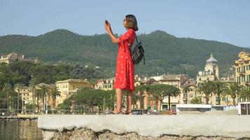 una donna con un vestito rosso scatta foto mentre viaggia in una località turistica di lusso in italia, europa. video