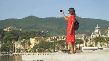 una donna con un vestito rosso scatta foto mentre viaggia in una località turistica di lusso in italia, europa. video