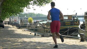 A couple running by boats on the river.