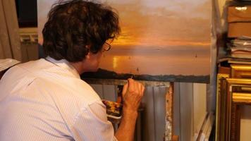 un artista pinta una pintura al óleo sobre lienzo dentro de su estudio de arte. video