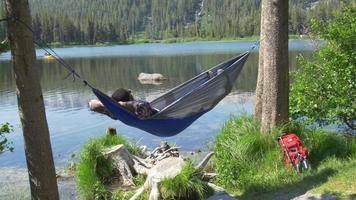 un uomo che riposa su un'amaca vicino a un lago di montagna. video