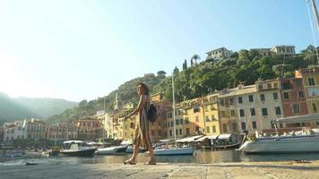 een vrouw die loopt met een hoed en een rugzak die reist in portofino, italië, een luxe vakantieoord in europa.