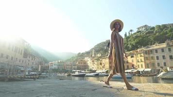 Eine Frau, die mit Hut und Rucksack in Portofino, Italien, einem Luxusresort in Europa, unterwegs ist. video