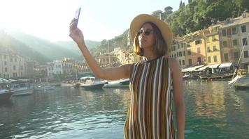 A woman takes selfies and uses facetime video calling in a luxury resort town in Europe.