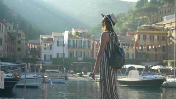 een vrouw die loopt met een hoed en een rugzak die reist in portofino, italië, een luxe vakantieoord in europa.