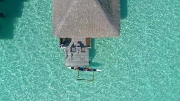 Aerial drone view of a man and woman couple in an overwater bungalow on Bora Bora tropical island. video