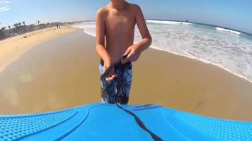 Vista pov de un niño poniéndose una correa para el bodyboard en las olas de la playa.