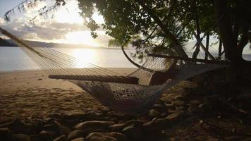 A woman rests in a hammock at sunset on a tropical island in Fiji.
