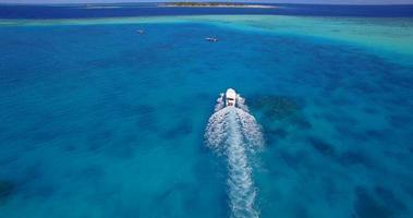 Vista aérea de un dron de una lancha a motor que va a una pintoresca isla tropical en las Maldivas. video