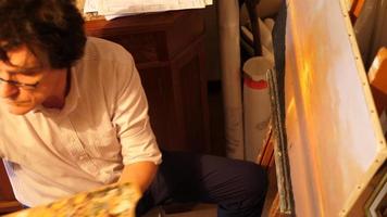 un artista pinta una pintura al óleo sobre lienzo dentro de su estudio de arte. video