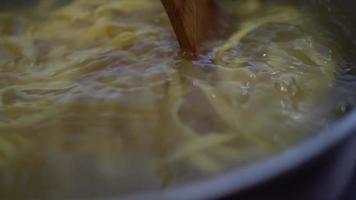 o cozinheiro prepara o macarrão enquanto mexe o macarrão é cozido em uma panela, em água quente video