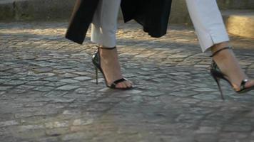 detalhes de close-up de pés de uma mulher andando com sapatos de salto alto em uma rua de paralelepípedos. - uso editorial apenas