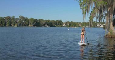 een jonge vrouw sup stand-up paddleboarding op een meer.