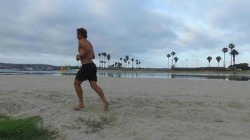 Tracking shot of a man jogging on the bay and beach.