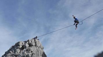 un homme essaie de s'équilibrer en slackline sur une corde raide dans les montagnes. video