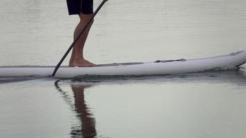 un hombre rema su tabla de remo de pie en un lago.