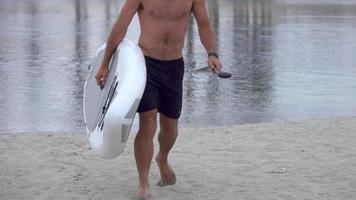 en man som bär och går med sin sup stand-up paddleboard i en sjö.