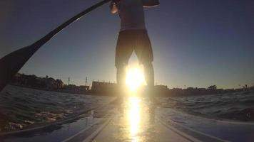 punto di vista di un uomo che rema un sup stand-up paddleboard su un lago al tramonto.