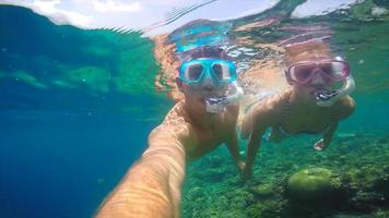 una pareja de hombre y mujer tomando un selfie mientras bucea sobre un arrecife de coral de una isla tropical. video